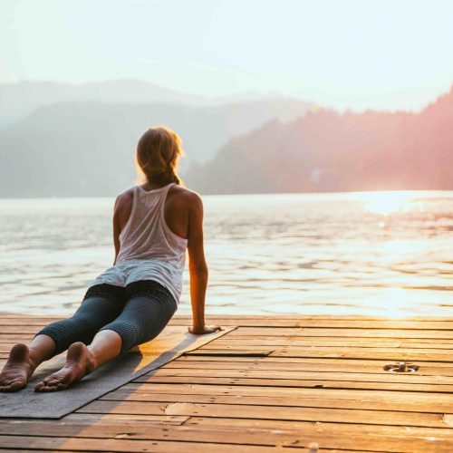 Beautiful woman practicing Yoga by the lake - Sun salutation series - Upward facing dog - Toned image
